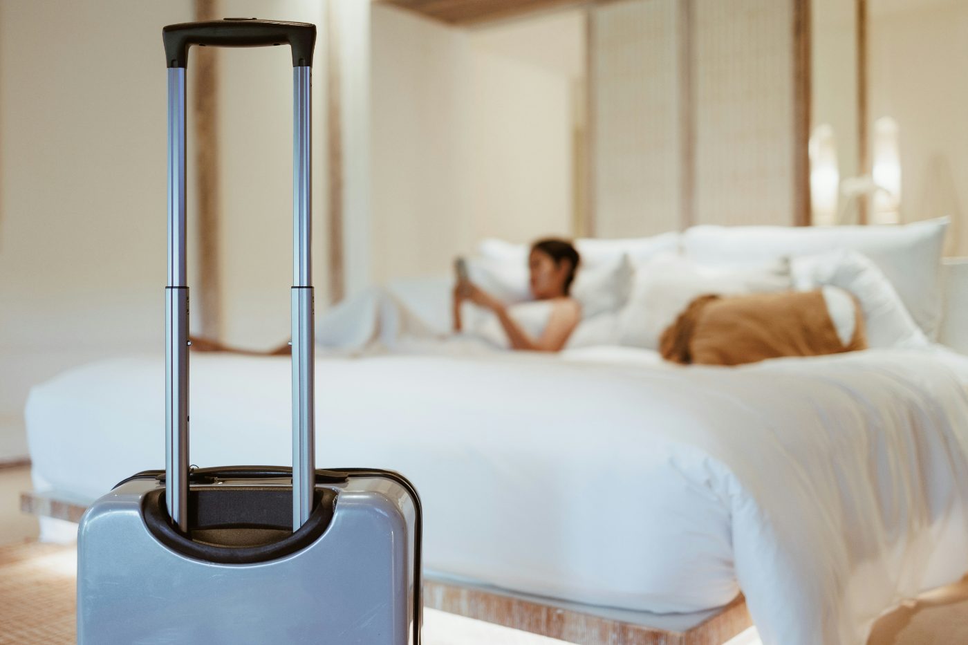 A guest relaxing on a crisp white bed beside a suitcase.